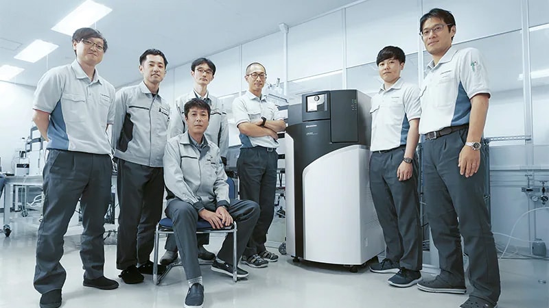 Kazuo Mukaibatake (front), Manager of the LCMS Group, MS Business Unit, Life Science Business Department, Analytical & Measuring Instruments Division, and members of the Analytical & Measuring Instruments Division around the LCMS-9030. In the photograph from the left are: Yohei Ukai, Assistant Manager in the Electronics Group, Research & Development Department; Atsushige Ikeda, Assistant Manager in the Software Group, Research & Development Department; Toru Shiohama, Deputy Manager in the Solution Development Group, MS Business Unit, Life Science Business Department; Yusuke Sakagoshi, Assistant Manager, Analyzer Group, Research & Development Department; Kazuma Maeda, Solution Development Group, MS Business Unit, Life Science Business Department; and Daisuke Okumura, Assistant Manager, LCMS Group, MS Business Unit, Life Science Business Department.