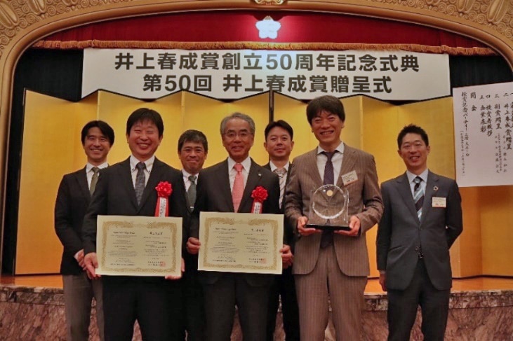 Shimadzu President and CEO Yasunori Yamamoto (center of front row) Holding the Award Certificate and Professor Takeshi Bamba, Medical Institute of Bioregulation, Kyushu University (left of front row)