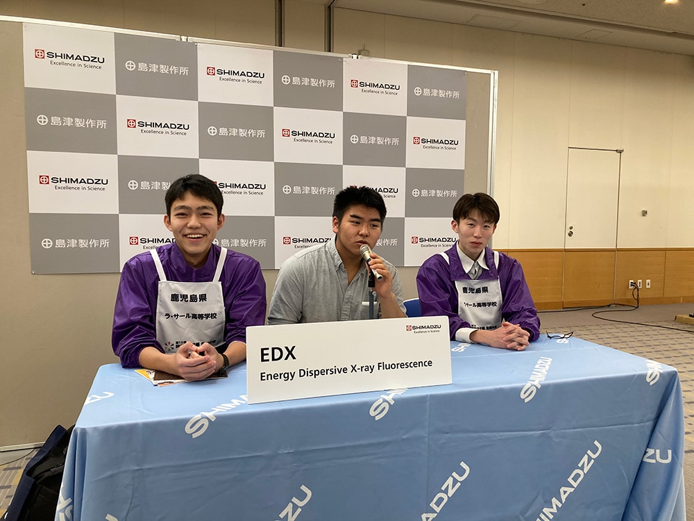 Competitors pose as presenters at a photo spot set up to look like a venue for a press conference