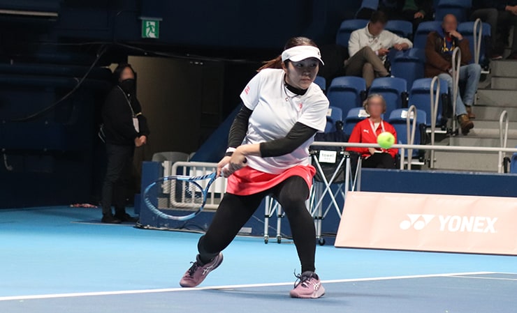 Left-handed Komokata stepping forward deeply with her left foot, attempting a backhand stroke