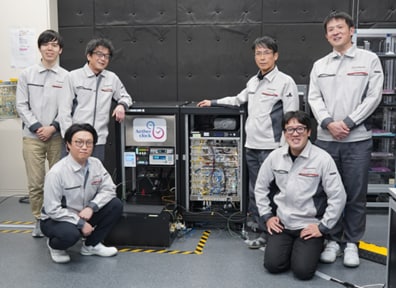 El reloj de red óptica Aetherclock OC020 y miembros del equipo de desarrollo. Fila de atrás, de izquierda a derecha: Kazuki Nigo, Tetsuo Furumiya, Koji Tojo, Bunta Matsuhana. Fila de adelante, de izquierda a derecha: Yuya Sakai, Takashi Muramatsu (ambos del Laboratorio de Investigación Tecnológica de Shimadzu Corporation).