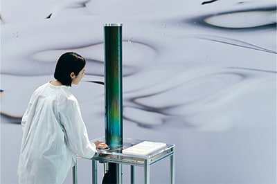 “Optical Rotation” is a work based on sugar’s ability to twist light. As light passes upward through a cylinder filled with sugar water, each color (wavelength) is twisted at a different angle. Turning the dial shifts a polarizing filter that allows only certain light to pass through, changing the colors visible to the viewer.